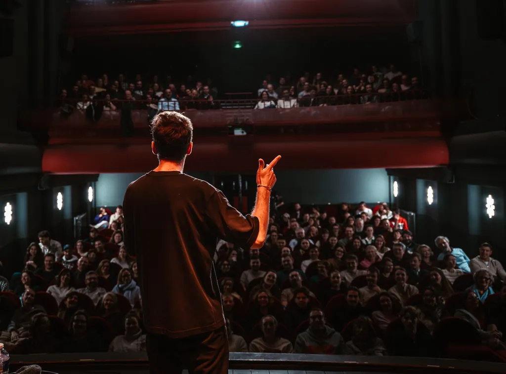 Stand-up comedian on stage facing a full theatre